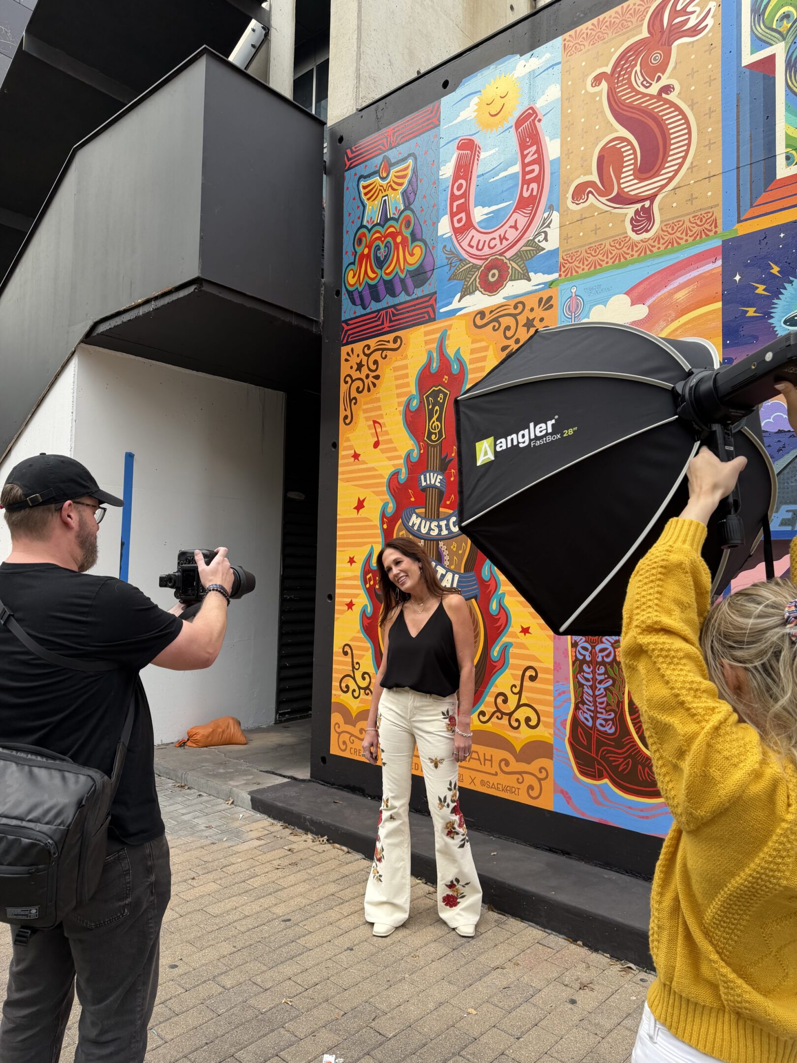 Photographer captures a woman posing against a colorful mural outdoors.