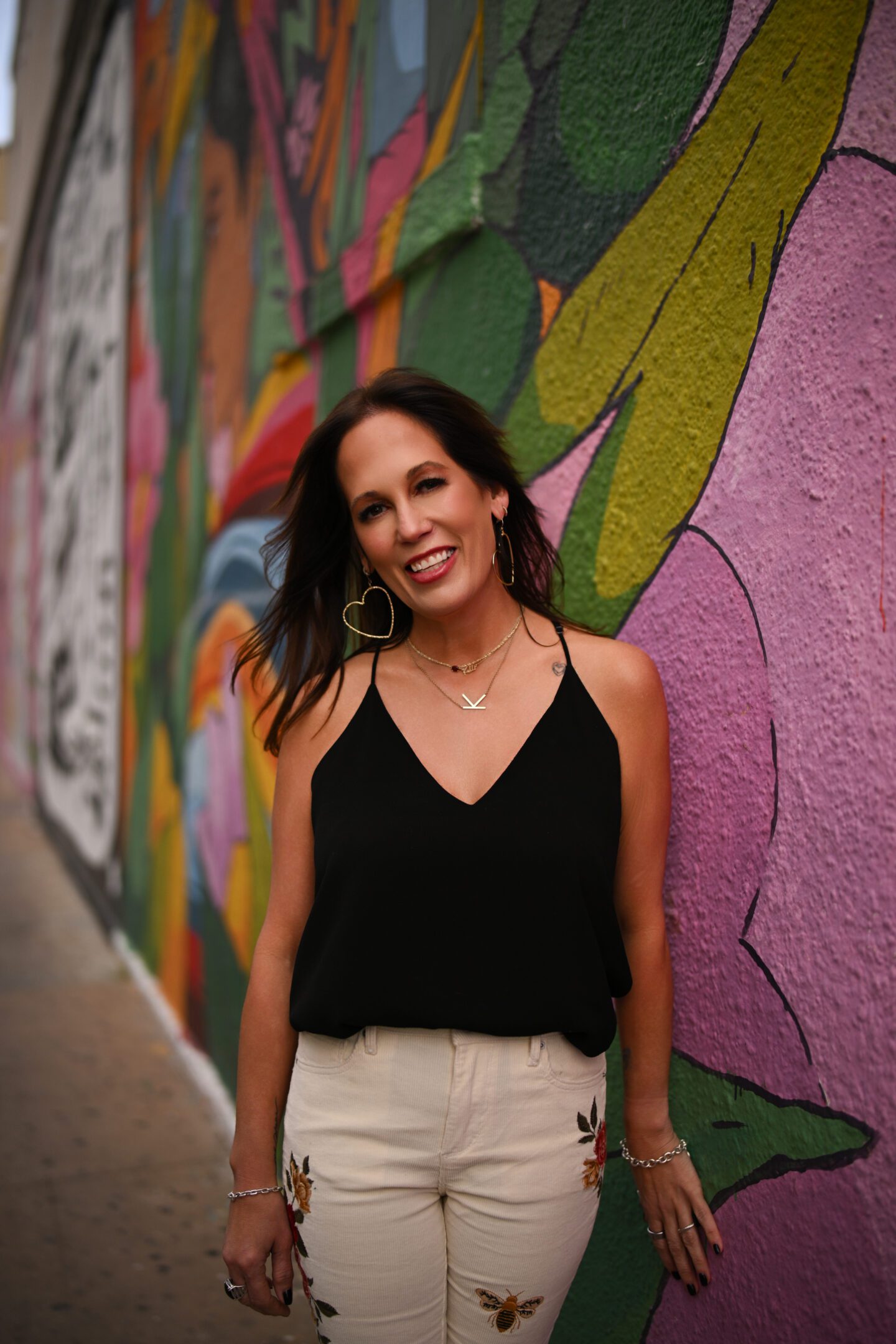 Woman posing happily against a colorful mural wall.
